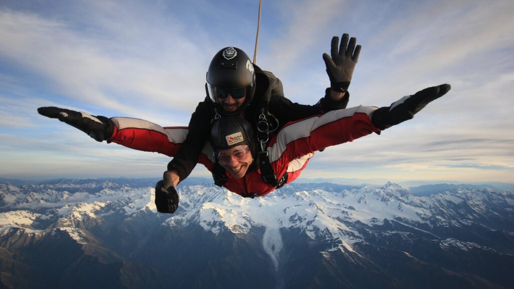 Skydiver descending over Fox Glacier with snowy peaks in background