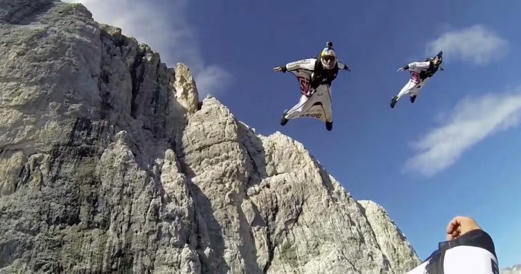 Wingsuit flyer in proximity flight near mountain cliff face